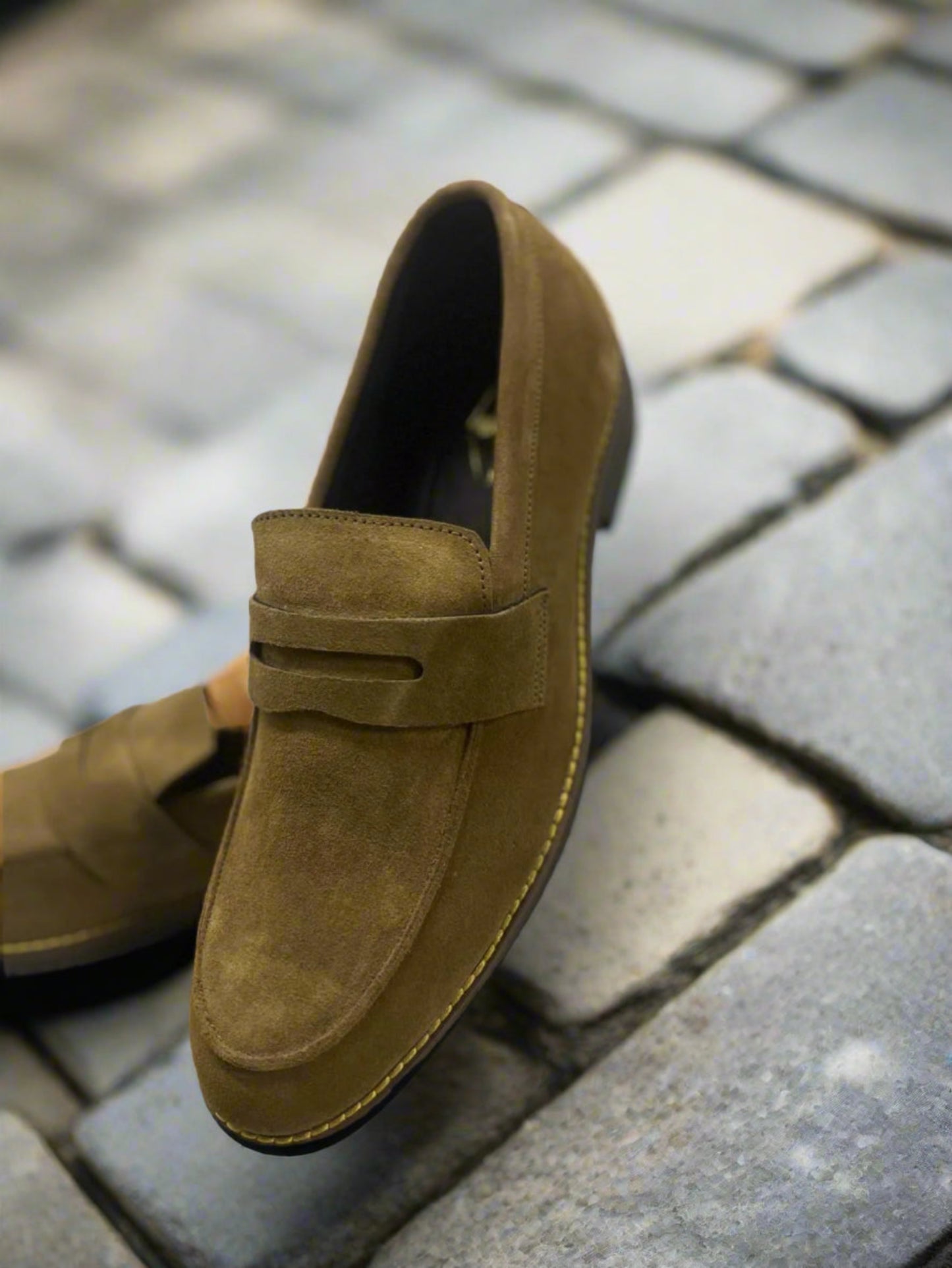 Brown suede loafer shoe on a light gray surface with a white background